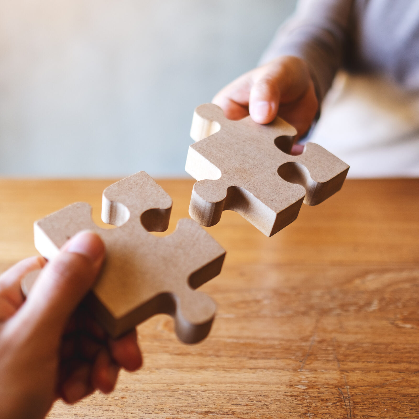 Closeup image of two people holding and putting a piece of wooden jigsaw puzzle together