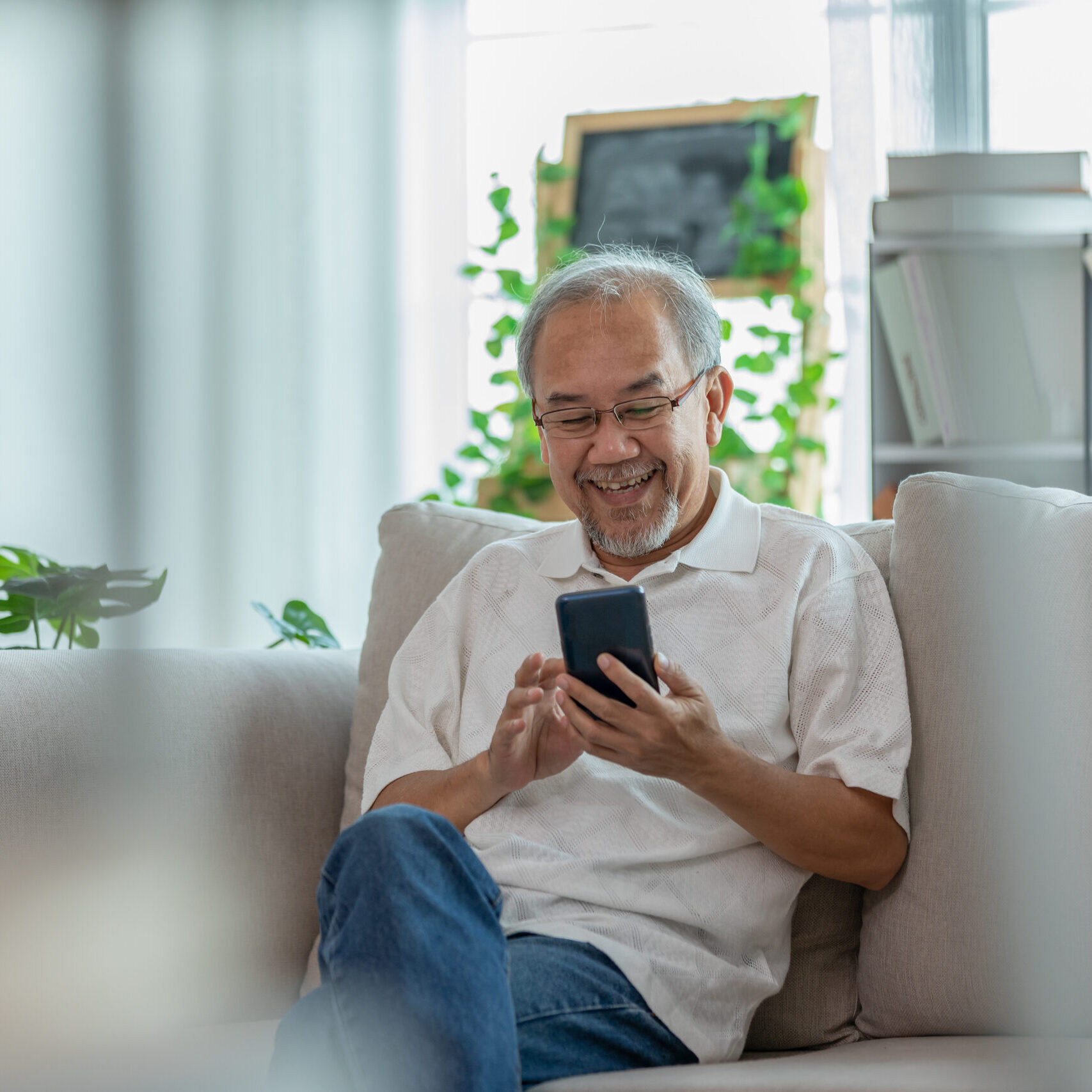 Happiness elderly asian man sitting on sofa using mobile phone and social media smile at home,Senior lifestyle at home concept