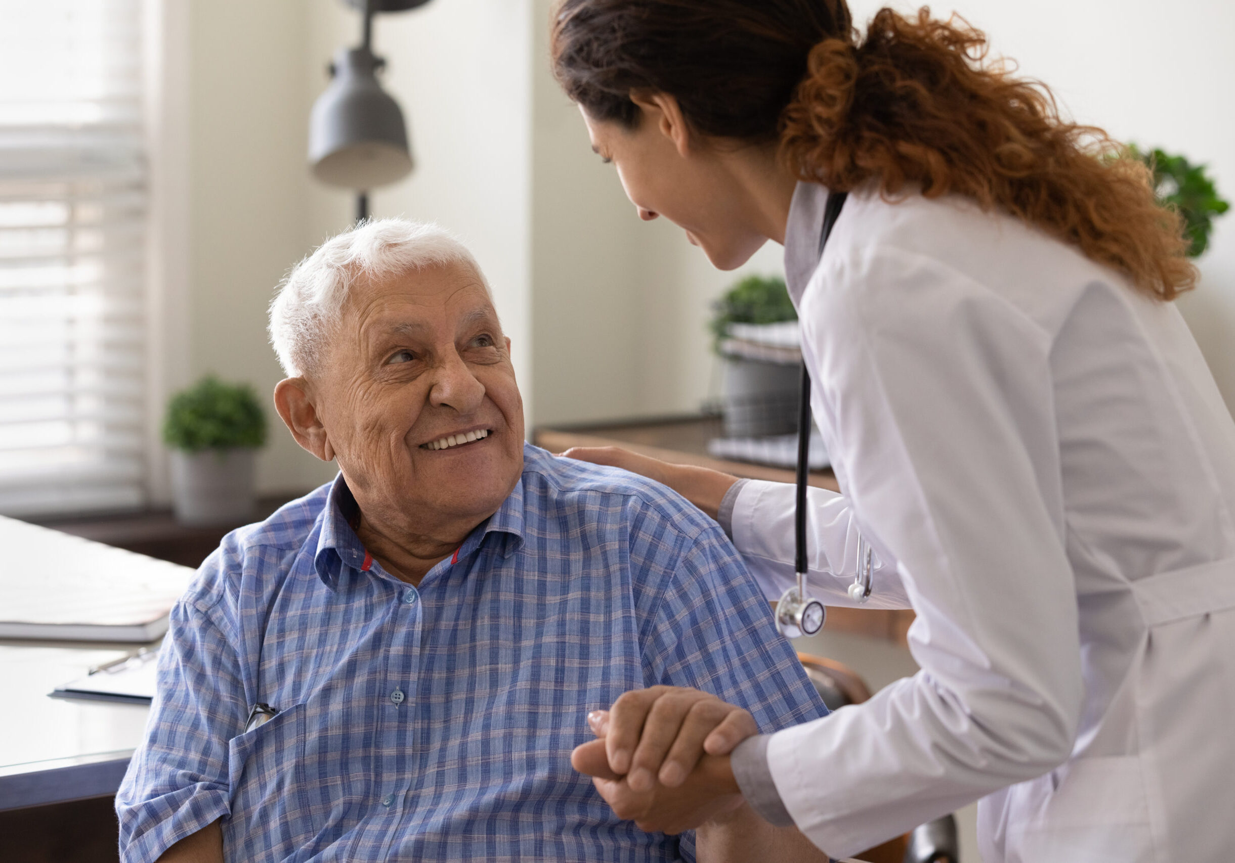 Close up caring nurse holding smiling mature patient hand at meeting in hospital, doctor caregiver wearing uniform comforting and supporting senior man, good news about treatment, empathy and care