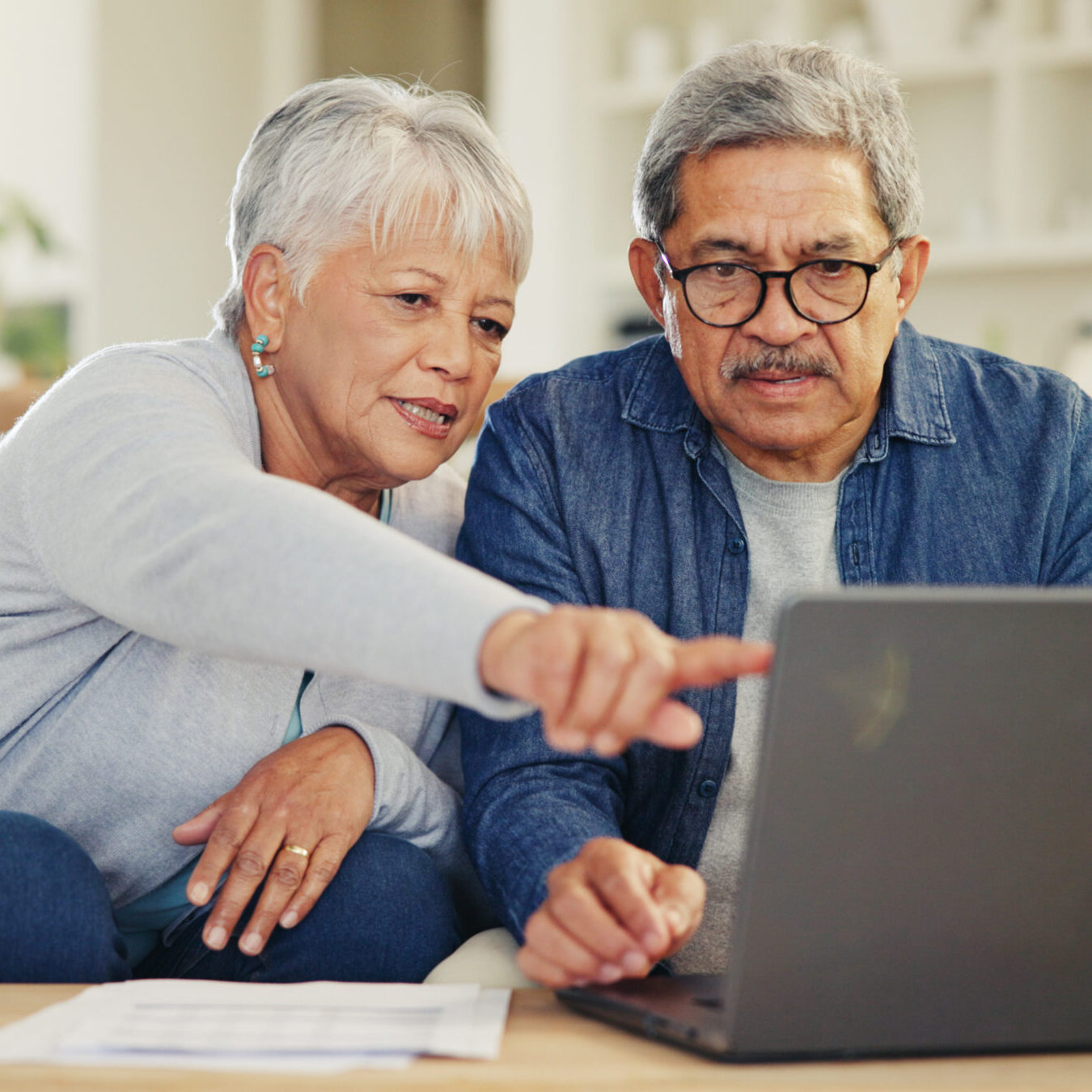 Senior, couple and planning on laptop in living room with document for finances, investment or retirement. Elderly man, woman and pointing by technology for online banking, account balance or savings.